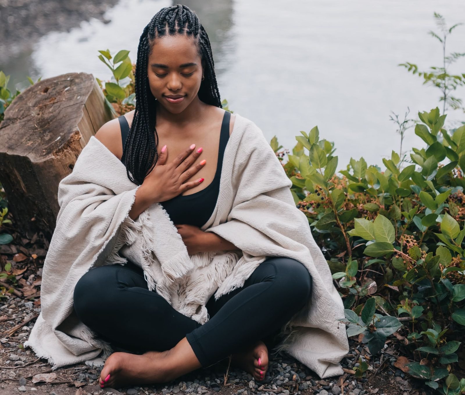 Une femme assise dans la nature, une main posée sur le cœur, les yeux fermés