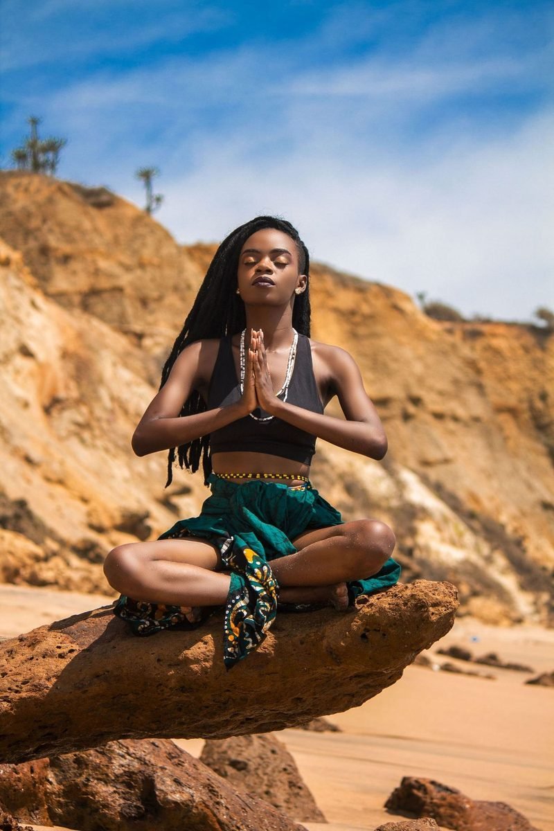 Une femme assise en méditation face à un ciel dégagé, bras ouverts