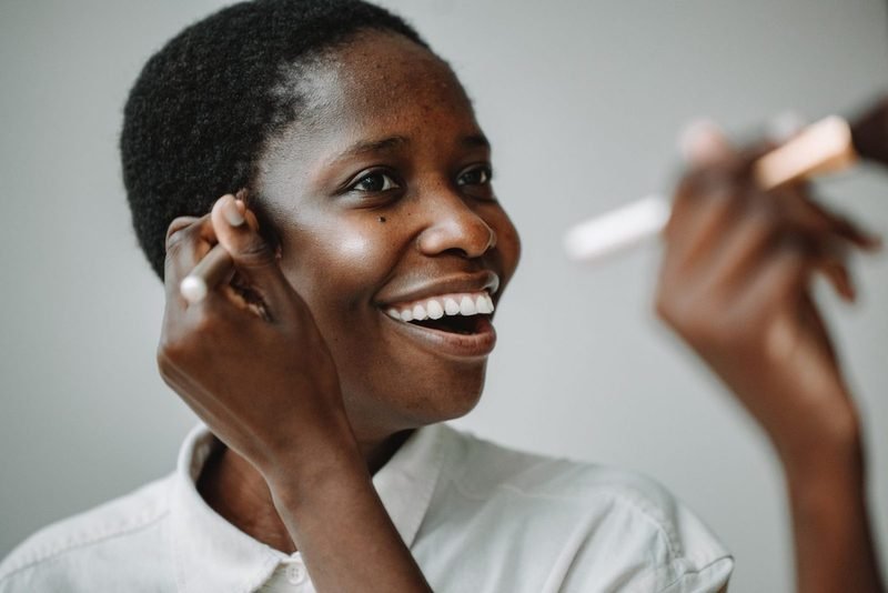 Une femme souriante applique elle-même son maquillage au pinceau